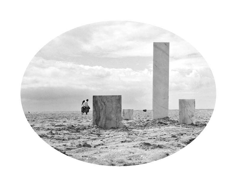 photograph of marble slates on sand at bech with passers by